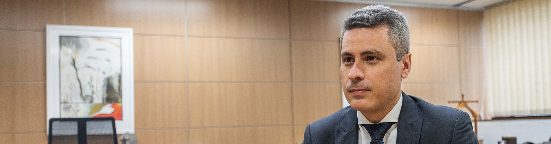 João Paulo Ferreira Machado, sentado numa sala com quadro à esqueda